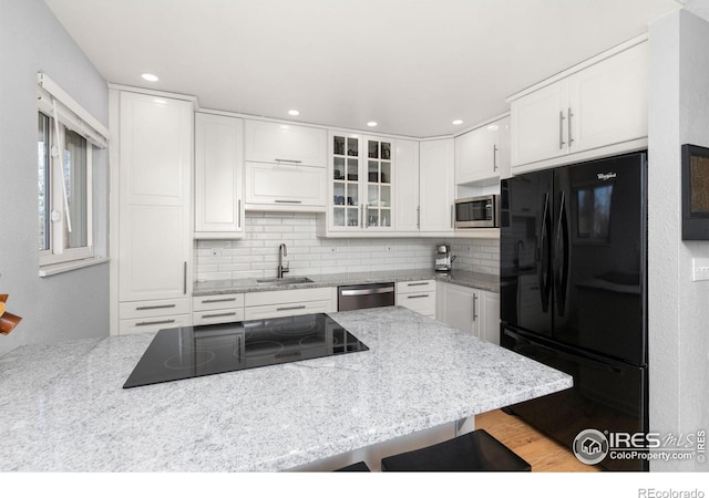 kitchen featuring white cabinetry, sink, a breakfast bar area, black appliances, and light stone countertops