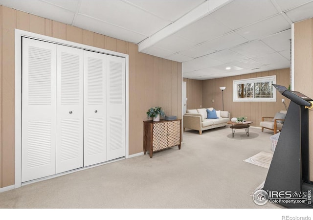 living area featuring carpet flooring, a paneled ceiling, and wood walls