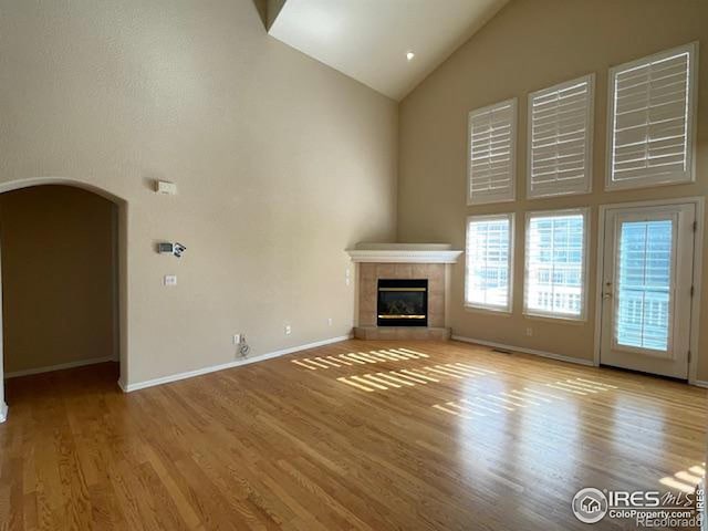 unfurnished living room with high vaulted ceiling, a tile fireplace, and light wood-type flooring