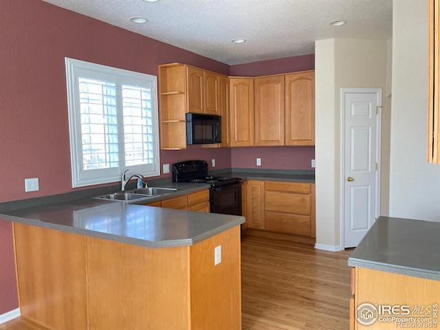 kitchen with kitchen peninsula, sink, light hardwood / wood-style flooring, and black appliances