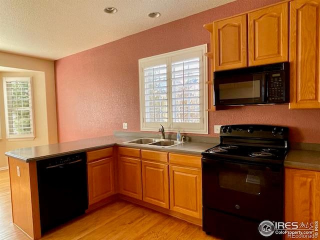 kitchen featuring sink, a textured ceiling, kitchen peninsula, light hardwood / wood-style floors, and black appliances