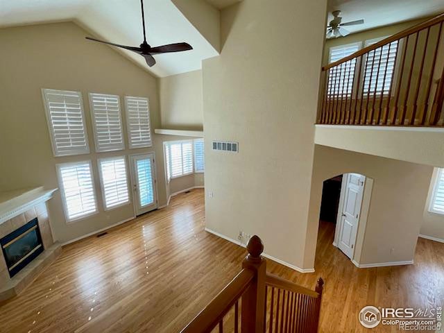 unfurnished living room featuring a tiled fireplace, light hardwood / wood-style flooring, high vaulted ceiling, and ceiling fan