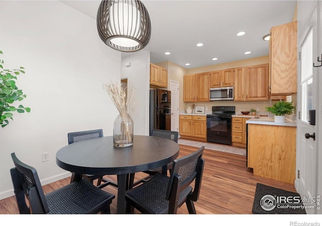 kitchen with light brown cabinetry, light hardwood / wood-style floors, and black appliances