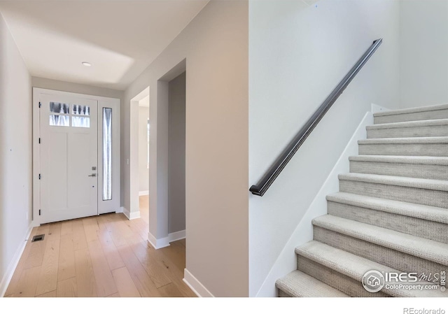 entryway with light wood finished floors, baseboards, visible vents, and stairway