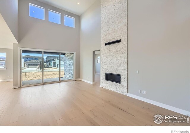 unfurnished living room featuring a stone fireplace, wood finished floors, and baseboards