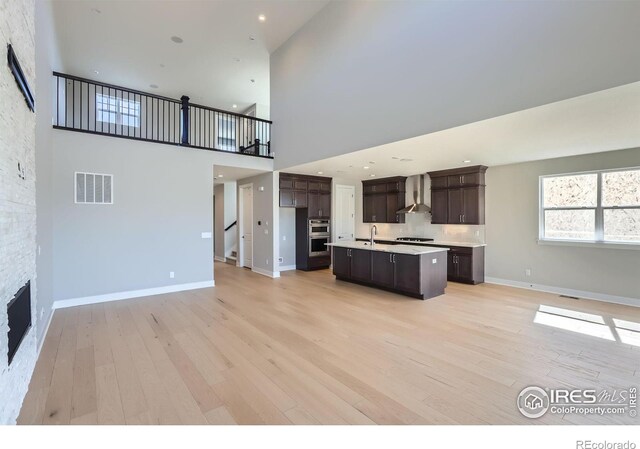 kitchen featuring light wood-type flooring, wall chimney exhaust hood, visible vents, and open floor plan