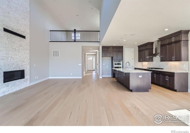 kitchen featuring a fireplace, gas stovetop, visible vents, light wood-style floors, and wall chimney range hood