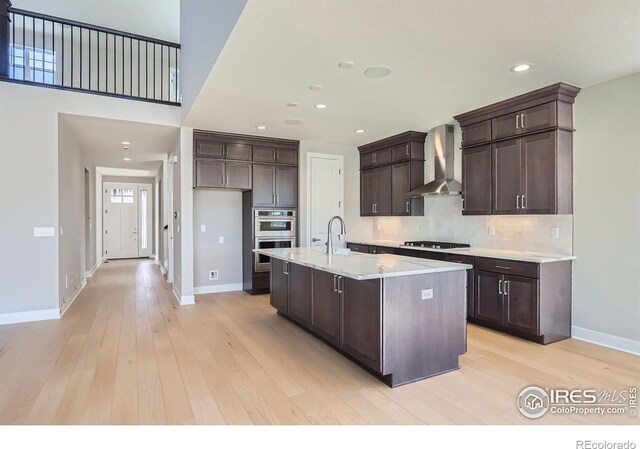 kitchen with dark brown cabinetry, wall chimney range hood, gas stovetop, and light wood-style flooring