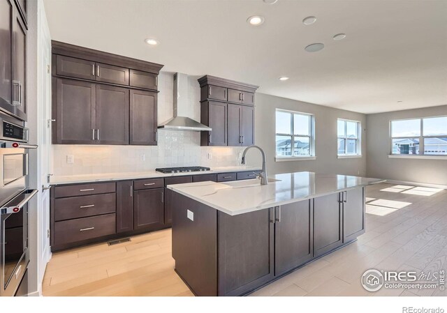 kitchen featuring tasteful backsplash, wall chimney exhaust hood, stainless steel double oven, gas stovetop, and a sink