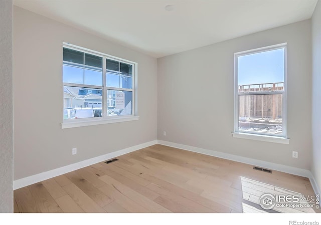 empty room featuring baseboards, wood finished floors, visible vents, and a healthy amount of sunlight