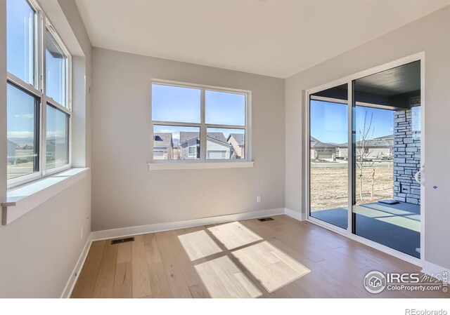 empty room featuring a healthy amount of sunlight, visible vents, and wood finished floors