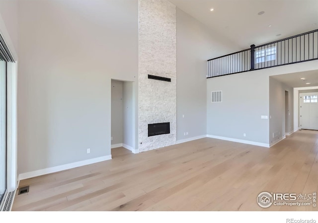 unfurnished living room featuring light wood-style floors, visible vents, a stone fireplace, and a high ceiling