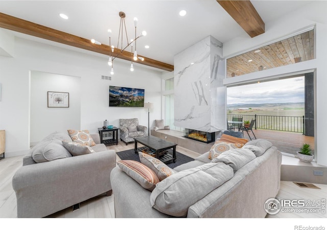 living room featuring a premium fireplace, an inviting chandelier, and beam ceiling