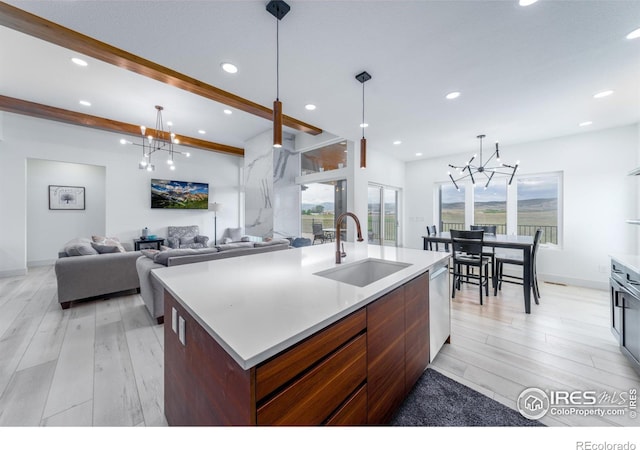 kitchen with pendant lighting, sink, light wood-type flooring, a center island with sink, and beam ceiling