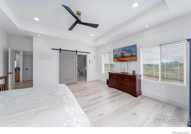 bedroom with a raised ceiling, a barn door, ceiling fan, and light hardwood / wood-style flooring