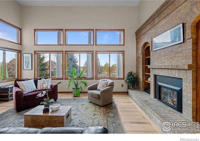 living room featuring light wood-type flooring, a high ceiling, a brick fireplace, and built in shelves