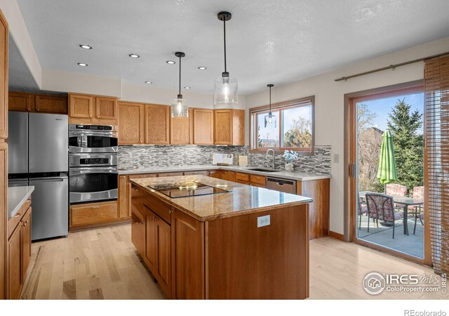 kitchen with stainless steel appliances, light stone counters, decorative light fixtures, a center island, and sink