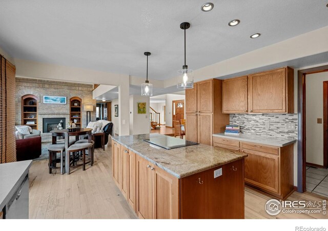 kitchen featuring a center island, light stone countertops, backsplash, black electric cooktop, and pendant lighting