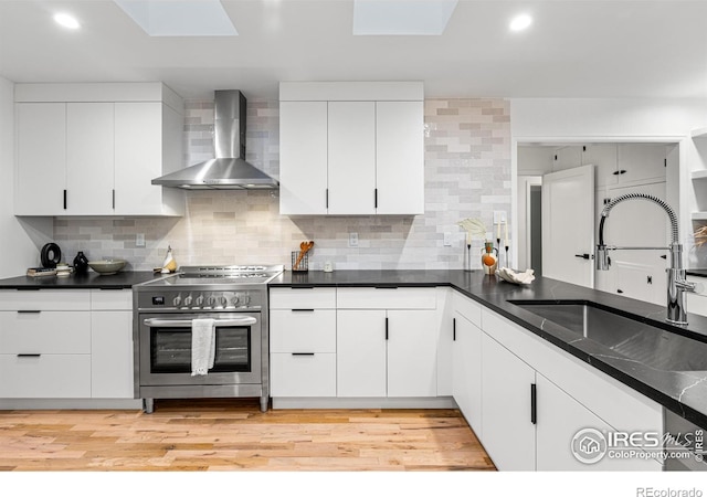 kitchen with sink, backsplash, white cabinets, stainless steel electric range oven, and wall chimney exhaust hood