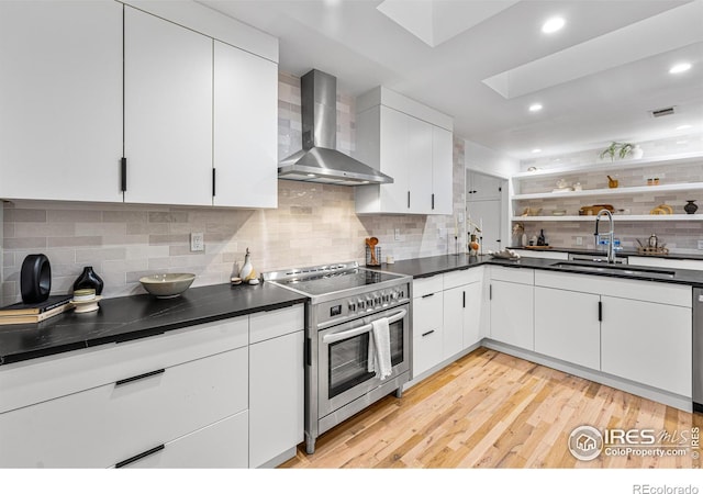 kitchen featuring a skylight, sink, white cabinets, wall chimney exhaust hood, and electric stove