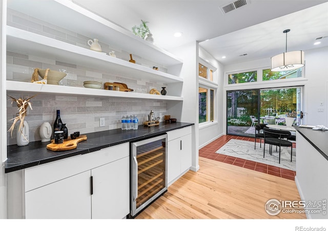 bar featuring light hardwood / wood-style flooring, hanging light fixtures, beverage cooler, decorative backsplash, and white cabinets