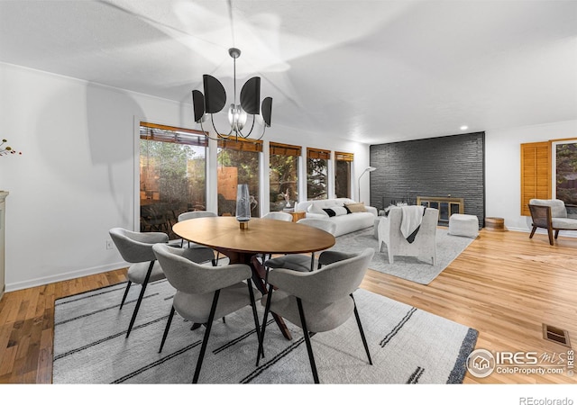 dining area featuring an inviting chandelier, a brick fireplace, and hardwood / wood-style flooring