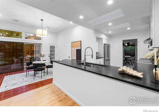 kitchen featuring a skylight, white cabinetry, stainless steel fridge, and decorative light fixtures