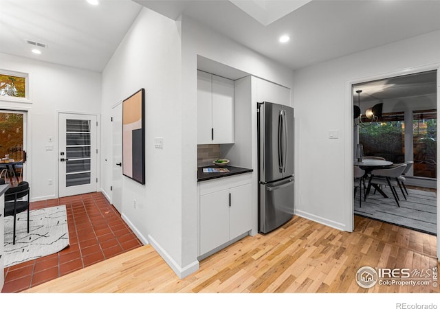 kitchen featuring white cabinets, hardwood / wood-style flooring, stainless steel fridge, and backsplash