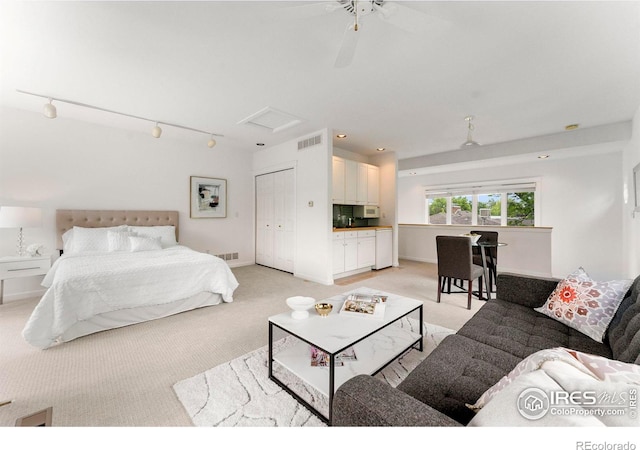 bedroom with ceiling fan, light colored carpet, rail lighting, and a closet