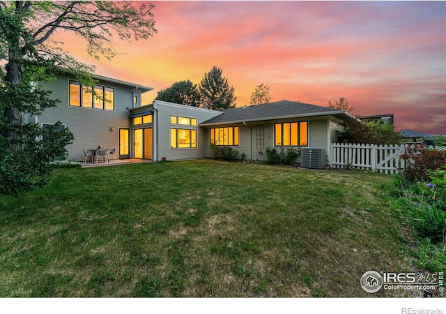 back house at dusk featuring a patio, a lawn, and central air condition unit