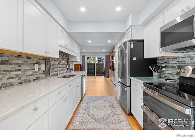 kitchen with sink, light hardwood / wood-style flooring, white cabinetry, stainless steel appliances, and decorative backsplash