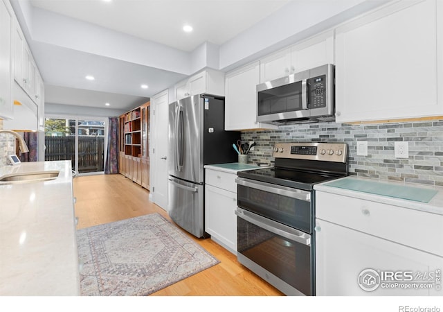 kitchen with appliances with stainless steel finishes, sink, light hardwood / wood-style flooring, and white cabinets