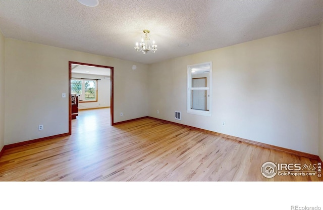 empty room with a textured ceiling, a notable chandelier, and light hardwood / wood-style floors