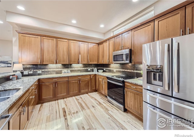 kitchen featuring stainless steel appliances, light stone countertops, backsplash, and light wood-type flooring