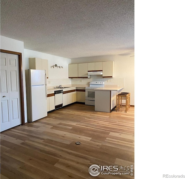 kitchen with a textured ceiling, light wood-type flooring, kitchen peninsula, white appliances, and backsplash