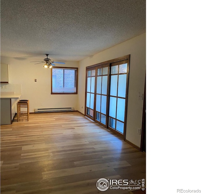 unfurnished living room featuring a baseboard heating unit, ceiling fan, a textured ceiling, and light wood-type flooring