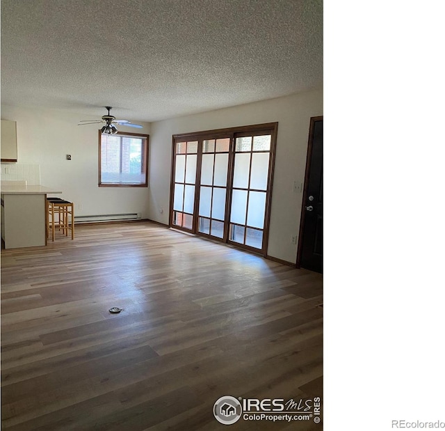 unfurnished living room featuring a baseboard heating unit, hardwood / wood-style floors, a textured ceiling, and ceiling fan