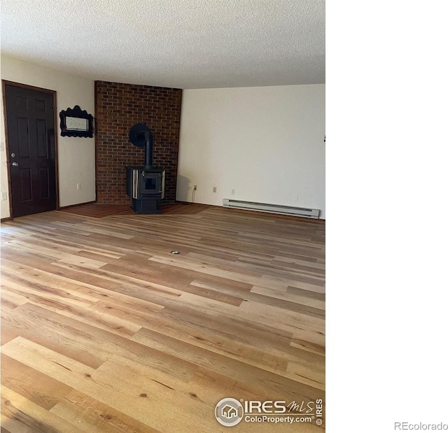 unfurnished living room with a baseboard heating unit, light hardwood / wood-style flooring, a textured ceiling, and a wood stove