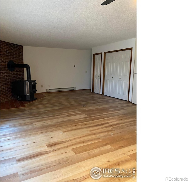 interior space featuring a wood stove, a baseboard heating unit, ceiling fan, a textured ceiling, and light hardwood / wood-style flooring