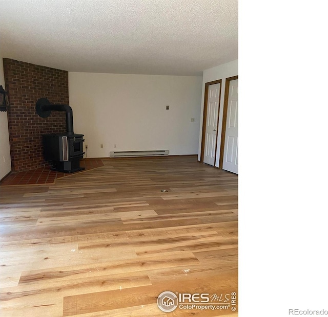 unfurnished living room featuring a baseboard heating unit, light hardwood / wood-style floors, a textured ceiling, and a wood stove