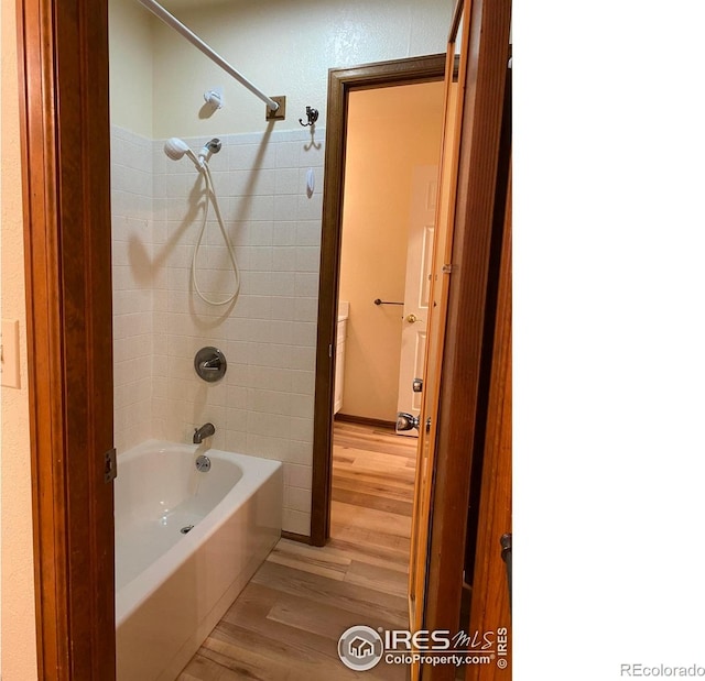 bathroom with tiled shower / bath, hardwood / wood-style floors, and toilet