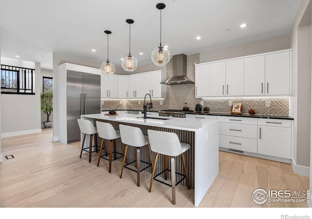 kitchen with pendant lighting, sink, stainless steel built in fridge, a center island with sink, and wall chimney exhaust hood