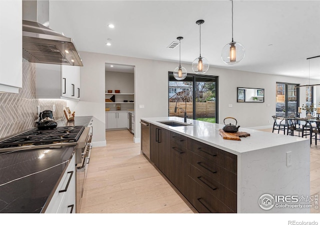 kitchen with pendant lighting, sink, an island with sink, white cabinets, and island exhaust hood