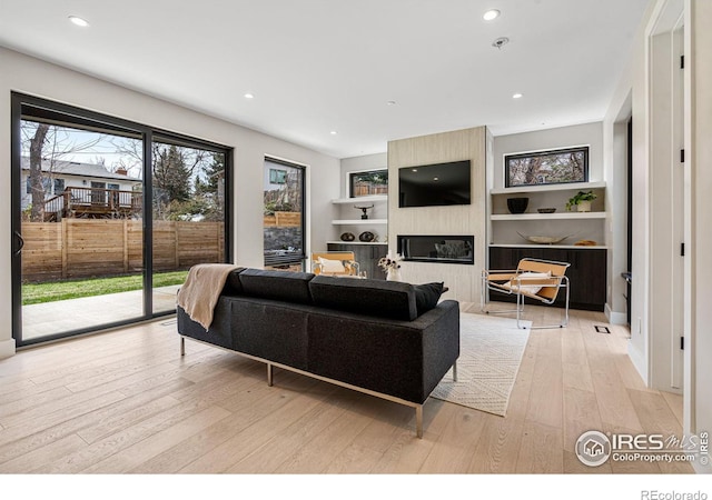 living room with built in features, a fireplace, and light wood-type flooring