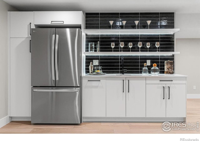 kitchen with stainless steel refrigerator, white cabinetry, sink, decorative backsplash, and light hardwood / wood-style flooring