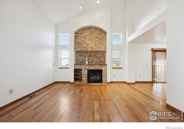 unfurnished living room with a stone fireplace, hardwood / wood-style floors, and high vaulted ceiling