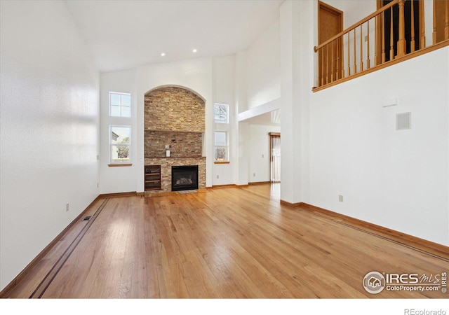 unfurnished living room with wood-type flooring, a high ceiling, baseboards, and a stone fireplace