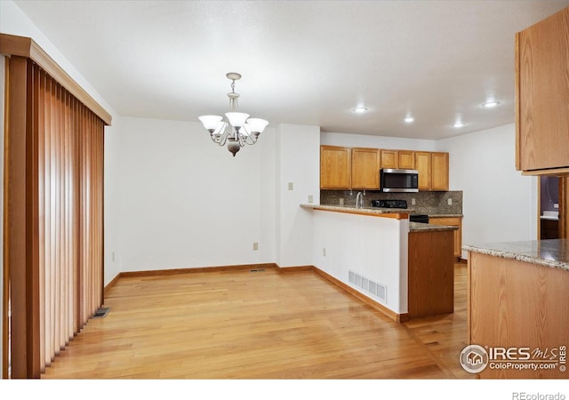 kitchen with stainless steel microwave, visible vents, decorative backsplash, light wood-style floors, and a chandelier