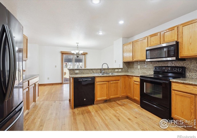 kitchen with a peninsula, black appliances, tasteful backsplash, and a sink