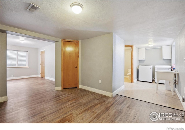 basement featuring a textured ceiling, light wood finished floors, washing machine and dryer, and visible vents